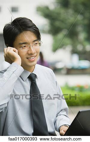 Stock Image - Businessman using laptop and cell phone outdoors. Fotosearch
