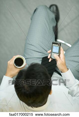 Stock Photography - Businessman using smart phone, holding cup of coffee. Fotosearch