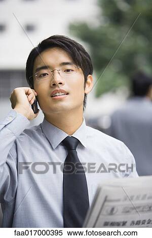 Businessman with newspaper using cell phone, looking at camera View Large Photo Image Stock Photography - Businessman with newspaper using cell phone, looking at camera. Fotosearch