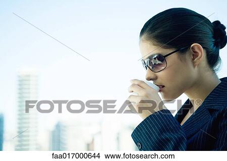 Picture - Businesswoman drinking hot drink, skyline in background. Fotosearch