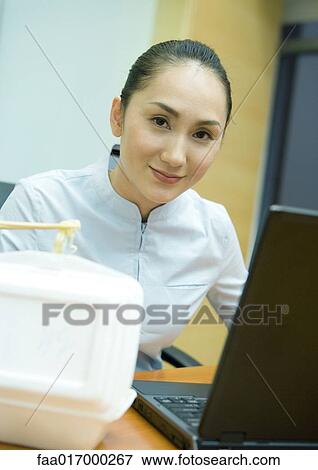 Businesswoman eating takeout food, and using laptop, smiling at camera View Large Photo Image Stock Photo - Businesswoman eating takeout food, and using laptop, smiling at camera. Fotosearch