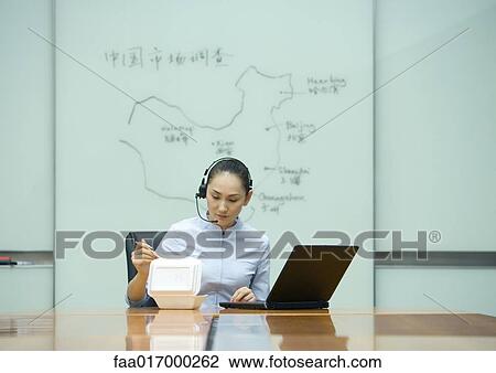 Businesswoman eating takeout food, wearing headset, and using laptop View Large Photo Image Stock Image - Businesswoman eating takeout food, wearing headset, and using laptop. Fotosearch