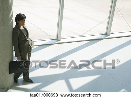 Stock Image - Businesswoman leaning against column, high angle view. Fotosearch