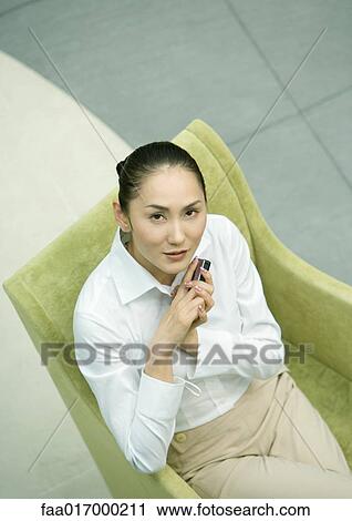 Businesswoman sitting in armchair, holding cell phone View Large Photo Image Stock Image - Businesswoman sitting in armchair, holding cell phone. Fotosearch