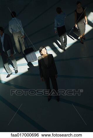 Stock Photograph - Businesswoman standing in beam of light with eyes closed while people walk by. Fotosearch