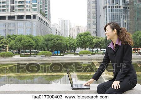 Businesswoman using laptop by water in office park View Large Photo Image Stock Image - Businesswoman using laptop by water in office park. Fotosearch