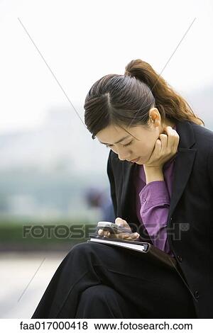 Businesswoman using messaging phone, leaning forward View Large Photo Image Stock Photo - Businesswoman using messaging phone, leaning forward. Fotosearch