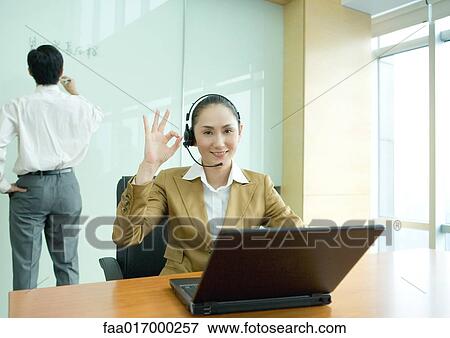 Businesswoman wearing headset and using laptop, making ok gesture View Large Photo Image Stock Photo - Businesswoman wearing headset and using laptop, making ok gesture. Fotosearch