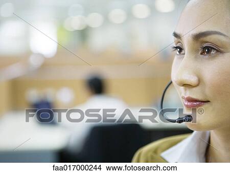 Businesswoman wearing headset in office, focus on foreground View Large Photo Image Picture - Businesswoman wearing headset in office, focus on foreground. Fotosearch