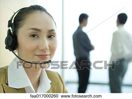 Businesswoman wearing headset, colleagues standing in background, portrait View Large Photo Image Stock Image - Businesswoman wearing headset, colleagues standing in background, portrait. Fotosearch