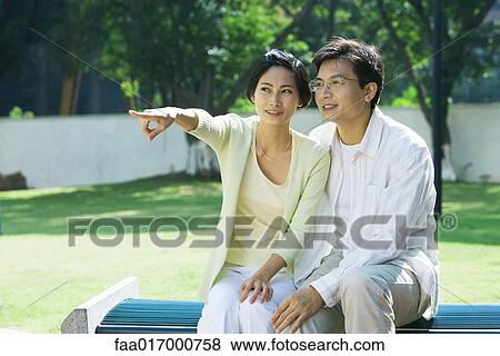 Couple sitting on bench, woman pointing out of frame View Large Photo Image Stock Photo - Couple sitting on bench, woman pointing out of frame. Fotosearch