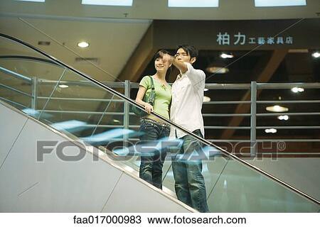 Couple taking escalator in shopping mall, man pointing out of frame View Large Photo Image Stock Image - Couple taking escalator in shopping mall, man pointing out of frame. Fotosearch