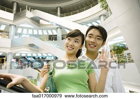 Couple taking escalator in shopping mall, woman waving View Large Photo Image Stock Photo - Couple taking escalator in shopping mall, woman waving. Fotosearch