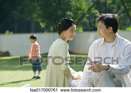 Couple talking while son plays in background View Large Photo Image Stock Image - Couple talking while son plays in background. Fotosearch