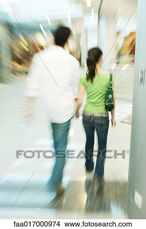 Couple walking in shopping mall, rear view, blurred motion View Large Photo Image Picture - Couple walking in shopping mall, rear view, blurred motion. Fotosearch