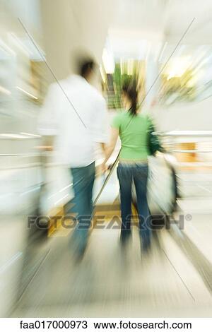 Stock Image - Couple walking toward escalator, blurred motion. Fotosearch