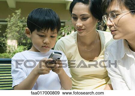 Stock Photo - Family, boy using cell phone while parents watch. Fotosearch