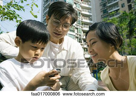 Stock Photograph - Family, boy using cell phone while parents watch. Fotosearch