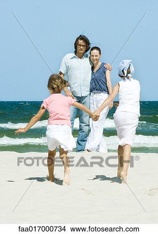 Family on beach, two girls walking hand in hand toward parents View Large Photo Image Picture - Family on beach, two girls walking hand in hand toward parents. Fotosearch