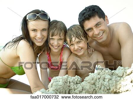 Stock Image - Family playing in sand at beach, smiling at camera, portrait. Fotosearch