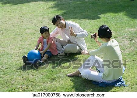 Family sitting on grass, woman taking photo of husband and son View Large Photo Image Stock Photo - Family sitting on grass, woman taking photo of husband and son. Fotosearch