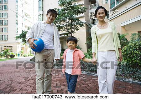 Stock Image - Family standing by apartment complex, smiling at camera, father holding ball. Fotosearch