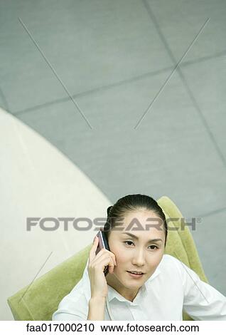 Stock Image - Female executive sitting in armchair using cell phone, high angle view. Fotosearch