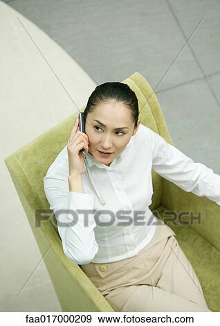 Stock Photo - Female executive sitting in armchair using cell phone, high angle view. Fotosearch