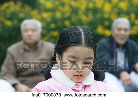 Stock Photo - Girl looking down, grandparents in blurred background. Fotosearch