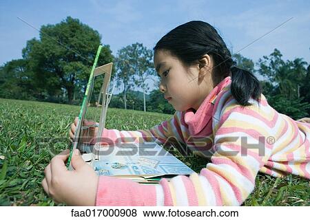 Stock Photo - Girl lying in grass with pop-up book. Fotosearch