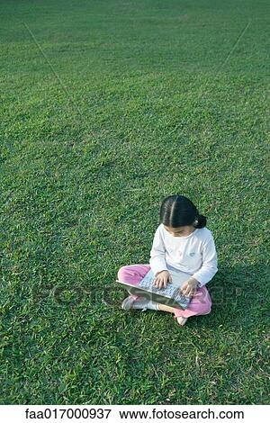 Stock Photo - Girl sitting in grass using laptop. Fotosearch