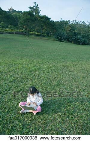 Stock Photo - Girl sitting in grass using laptop. Fotosearch