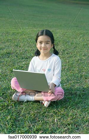 Girl sitting in grass using laptop View Large Photo Image Stock Photo - Girl sitting in grass using laptop. Fotosearch