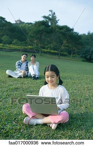 Girl sitting in grass using laptop, parents sitting in background View Large Photo Image Stock Photograph - Girl sitting in grass using laptop, parents sitting in background. Fotosearch