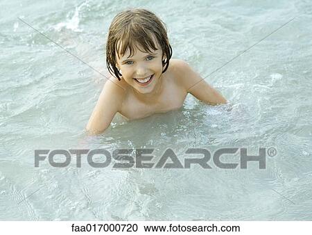 Stock Image - Girl wading in shallow water, smiling at camera. Fotosearch
