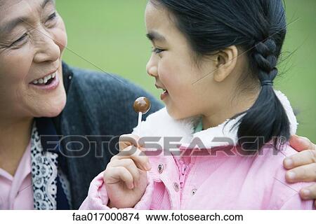 Picture - Girl with grandmother, eating lollipop. Fotosearch