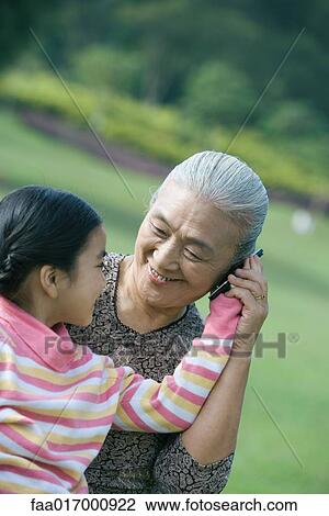 Stock Image - Girl with grandmother, holding cell phone to ear. Fotosearch