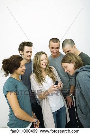 Stock Photo - Group of young adult and teenage friends looking at cell phone, white background. Fotosearch