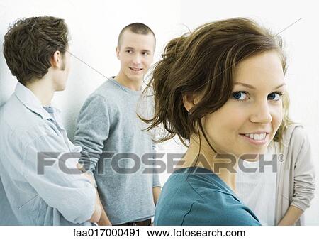 Stock Image - Group of young adults, woman in foreground looking over shoulder at camera. Fotosearch
