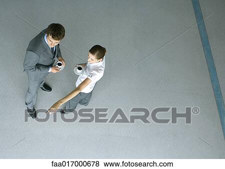 Stock Photo - Male and female associates having coffee, woman pointing, full length, high angle view. Fotosearch