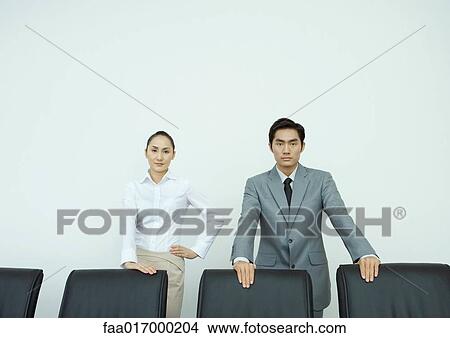 Male and female executives standing with hands on backs of chairs, looking at camera, portrait View Large Photo Image Picture - Male and female executives standing with hands on backs of chairs, looking at camera, portrait. Fotosearch