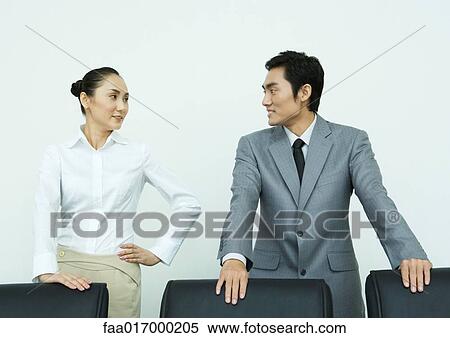Male and female executives standing with hands on backs of chairs, looking at each other View Large Photo Image Stock Photography - Male and female executives standing with hands on backs of chairs, looking at each other. Fotosearch
