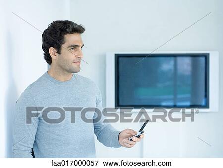 Man holding out cell phone, looking away, widescreen TV in background View Large Photo Image Stock Photo - Man holding out cell phone, looking away, widescreen TV in background. Fotosearch