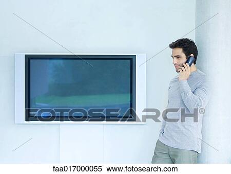 Man leaning against wall using phone, next to widescreen TV View Large Photo Image Stock Photography - Man leaning against wall using phone, next to widescreen TV. Fotosearch