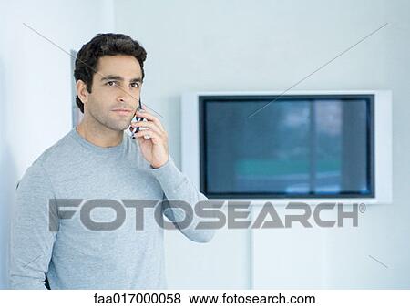 Man using cell phone, widescreen TV in background View Large Photo Image Stock Photo - Man using cell phone, widescreen TV in background. Fotosearch