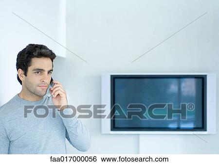Stock Photograph - Man using phone, widescreen TV in background. Fotosearch