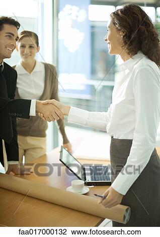 Stock Image - Mature female architect shaking hands with young male client. Fotosearch