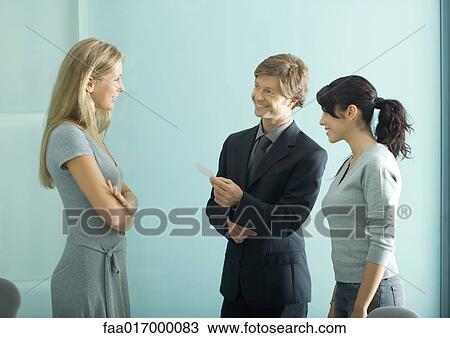 Stock Image - Mature man and teenage girl facing young female professional, man holding business card. Fotosearch