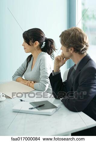 Picture - Mature man and teenage girl sitting at table, looking out of frame. Fotosearch
