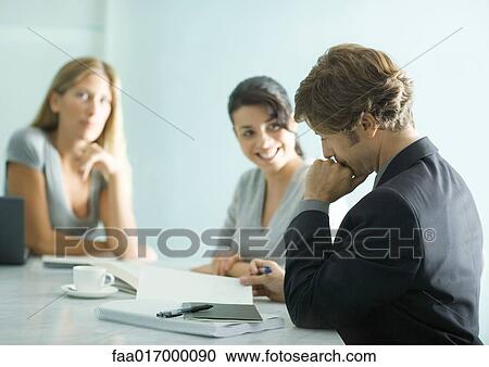Stock Image - Mature man sitting at table with teenage girl and young female professional, reading document. Fotosearch